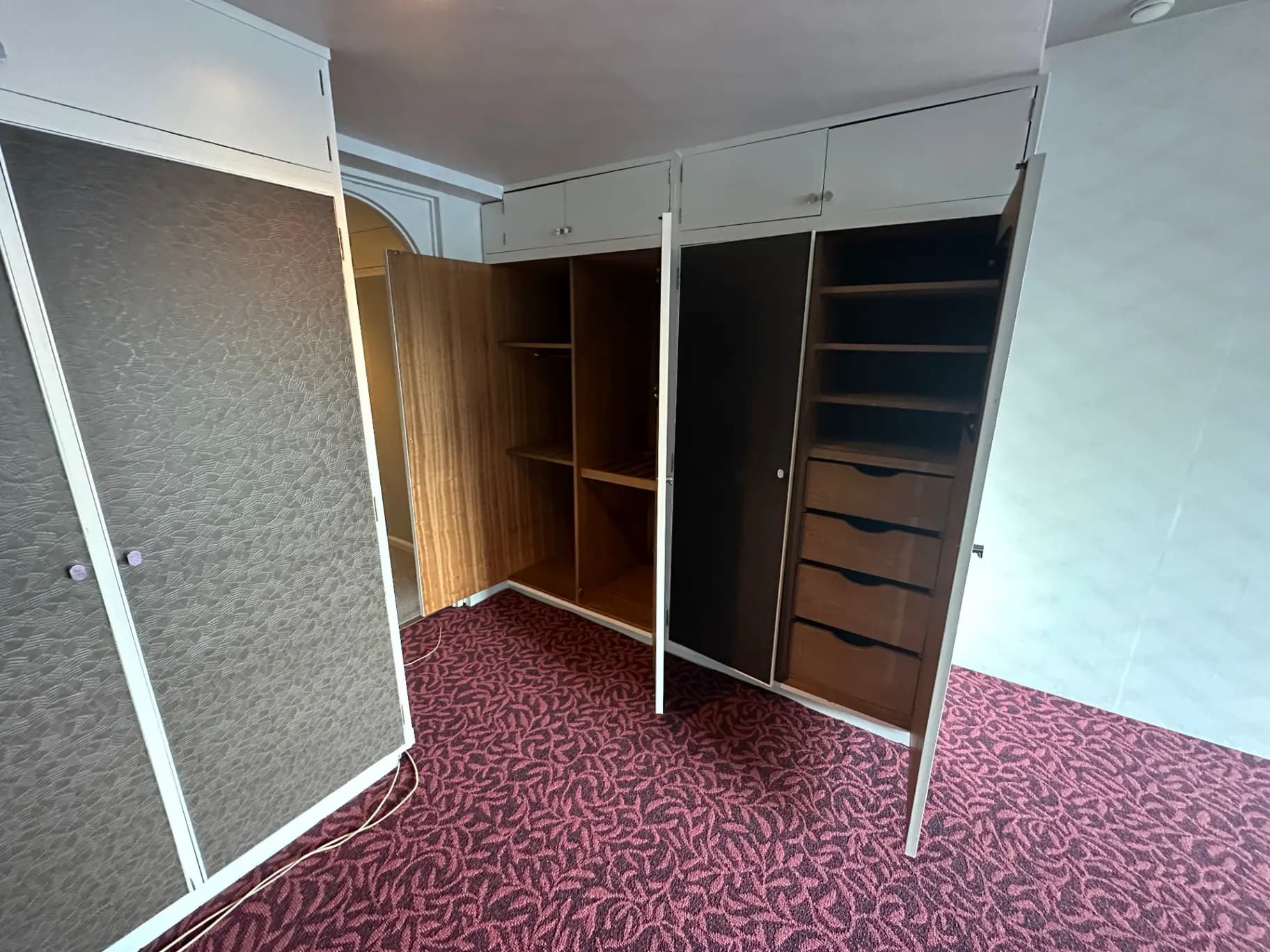 広々としたクローゼットスペース、木製の棚と引き出し、茶色のカーペットが敷かれた部屋