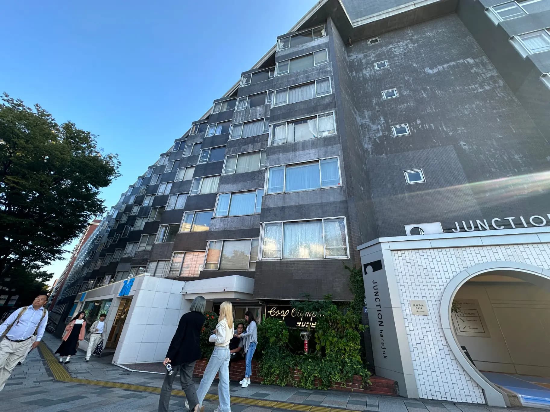 都会的なアパートの外観、幹線道路に面した建物エントランス、歩行者と夕暮れの空