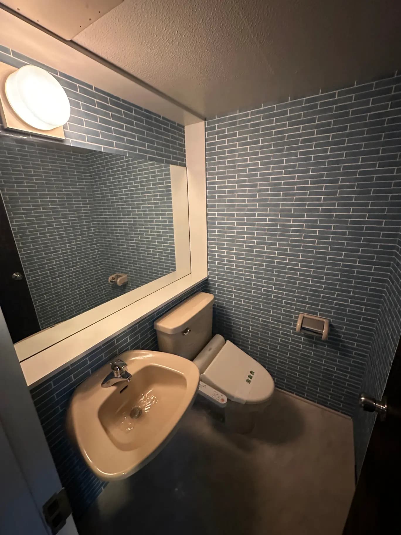 コンパクトなトイレと洗面台、青いタイルの壁とベージュの設備が特徴的なバスルームのインテリア