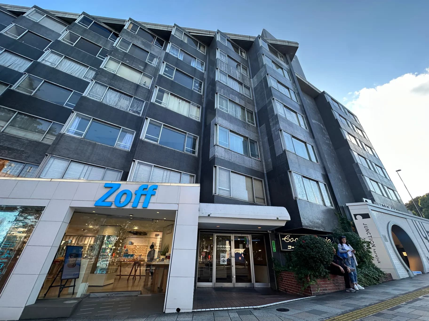Zoffメガネ店の外観と周辺商業施設、青空の下の現代的な建築スタイル