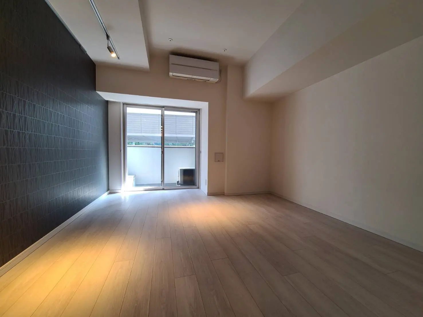 シンプルな内装の空き部屋、木目調のフローリング、大きな窓と天井照明