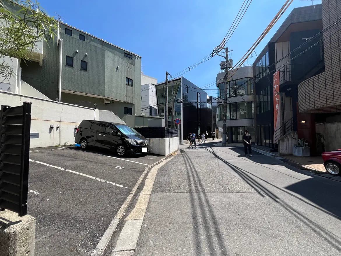 - 都会的な風景の路地、モダンな建物や駐車場が並び、青空が広がる光景