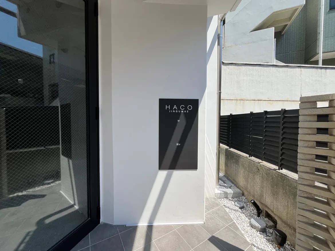 - モダンなデザインの建物の入口、黒い看板に「HACO Jingumae」と記載されたエントランスの外観