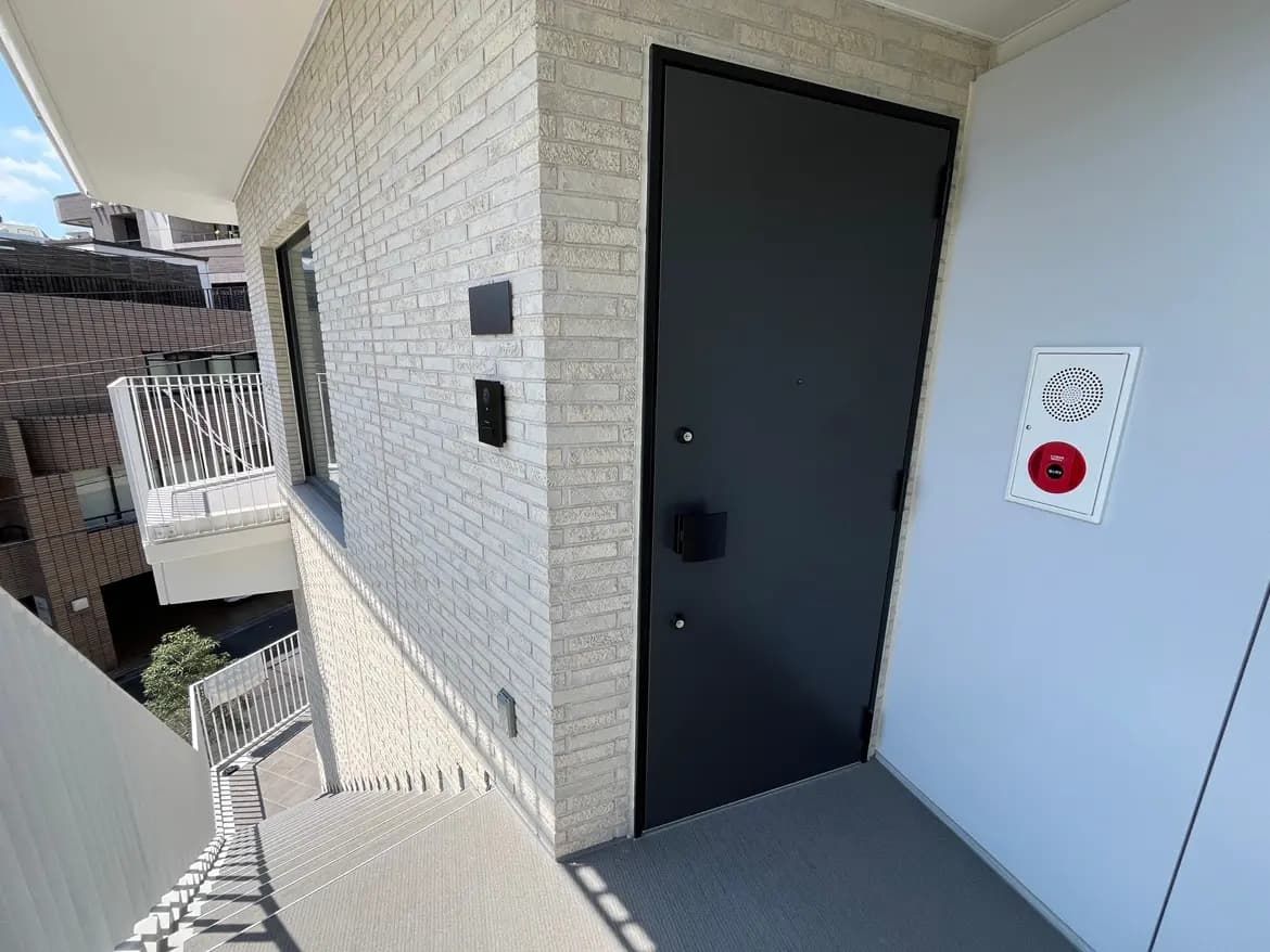 - モダンなデザインのマンションの玄関、黒いドアと隣接したインターホン、明るい外の景色が見える外観