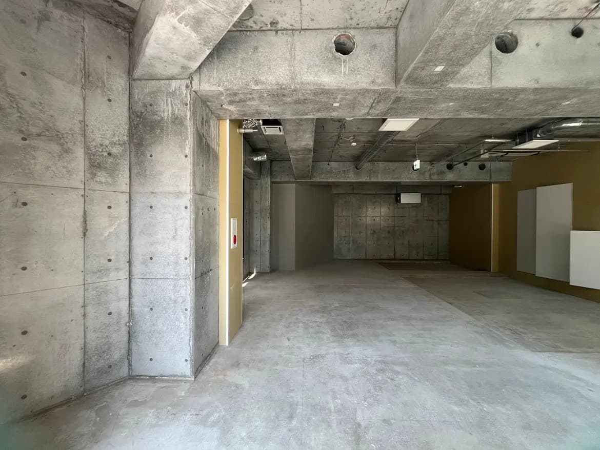 - コンクリートの壁と床のある広々とした空間、四角い天井、シンプルなデザインのオフィスや作業スペース