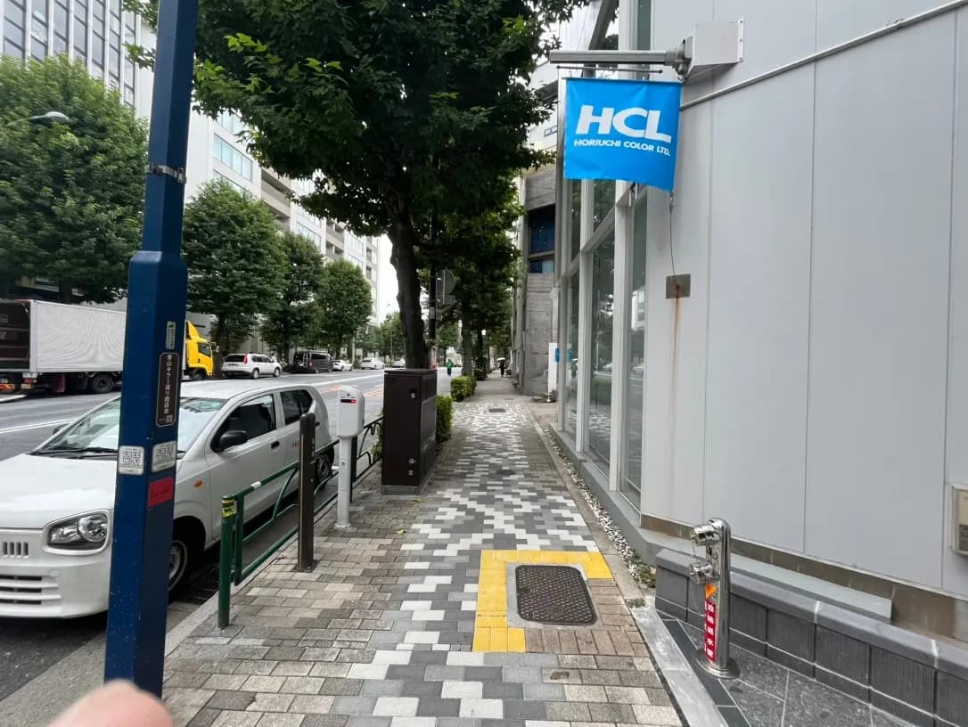 都会の歩道沿いの風景、並木道と企業の旗、駐車中の白い自動車、クリーンで整備された市街地