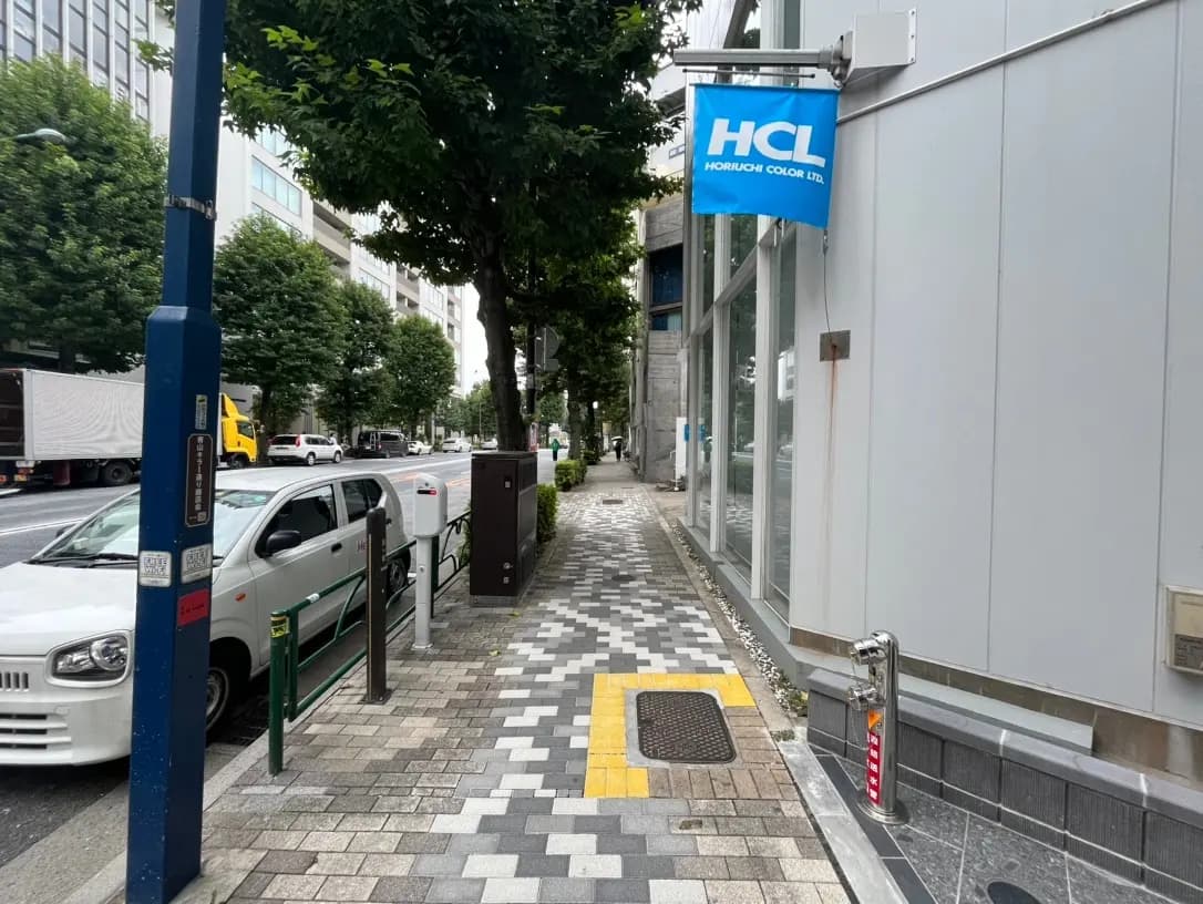 都会の歩道と緑の樹木、清潔な街並み、通りを走る車とHCLの看板が見える景観