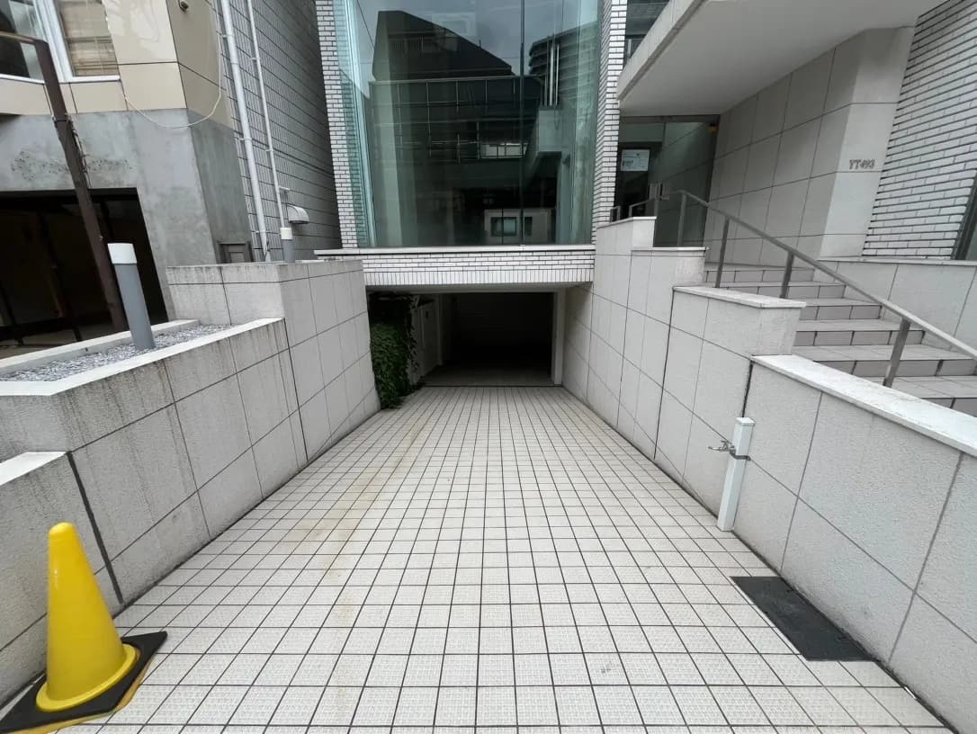 現代的な都市型ビルの屋外通路、タイル貼りの床と壁、手すりつきの階段と黄色い安全コーン