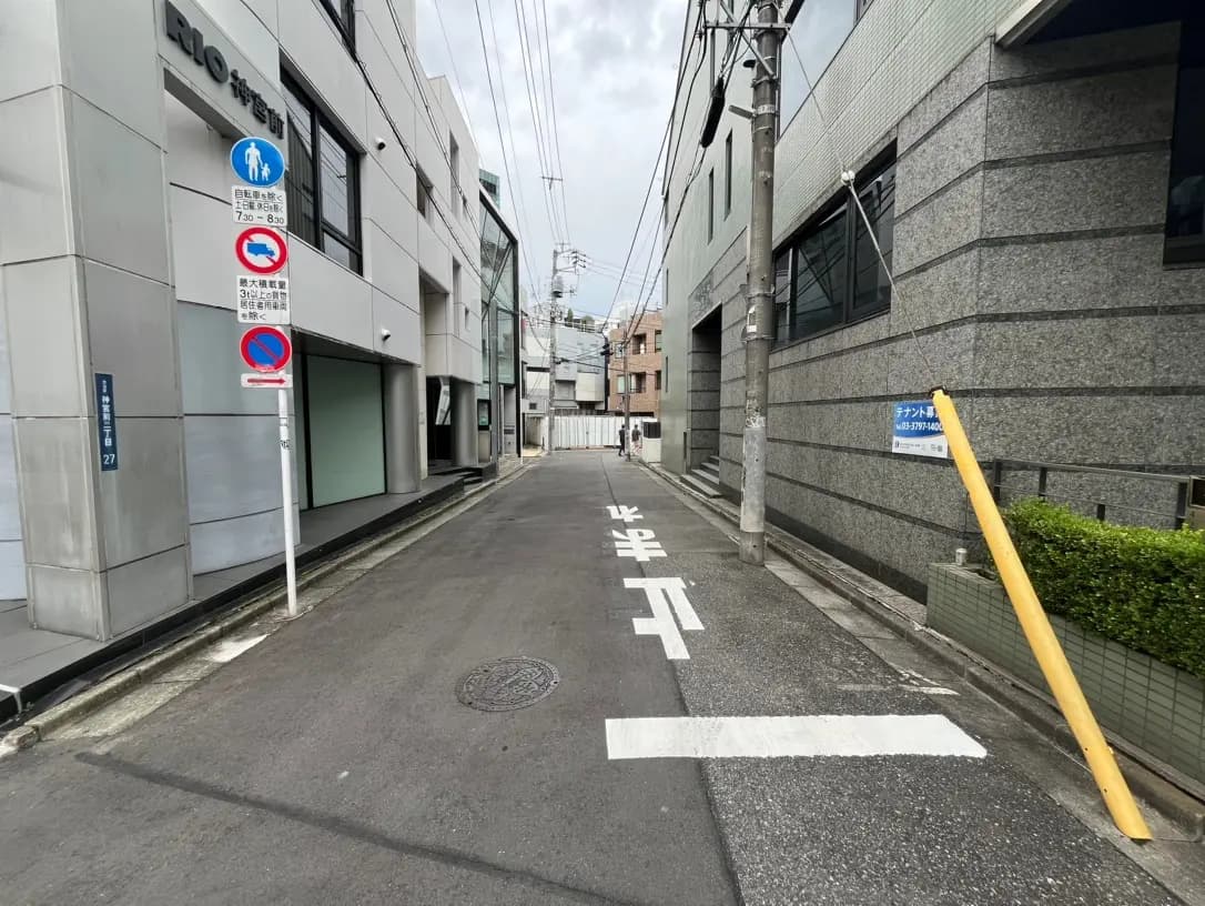 静かな住宅街のアスファルト道路、昼間の曇り空、交通標識と電柱が並ぶ景色
