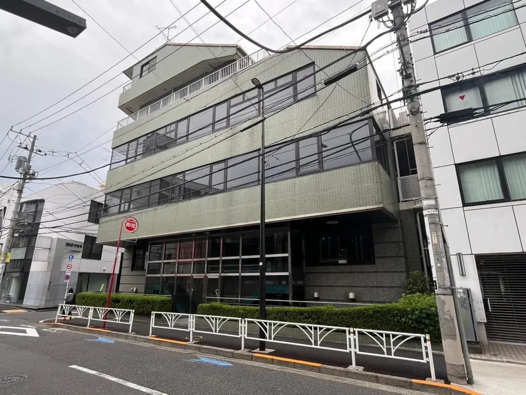 市街地に位置する現代的な多階建てビル、クリーム色外壁、ガラス窓、路上駐車スペース