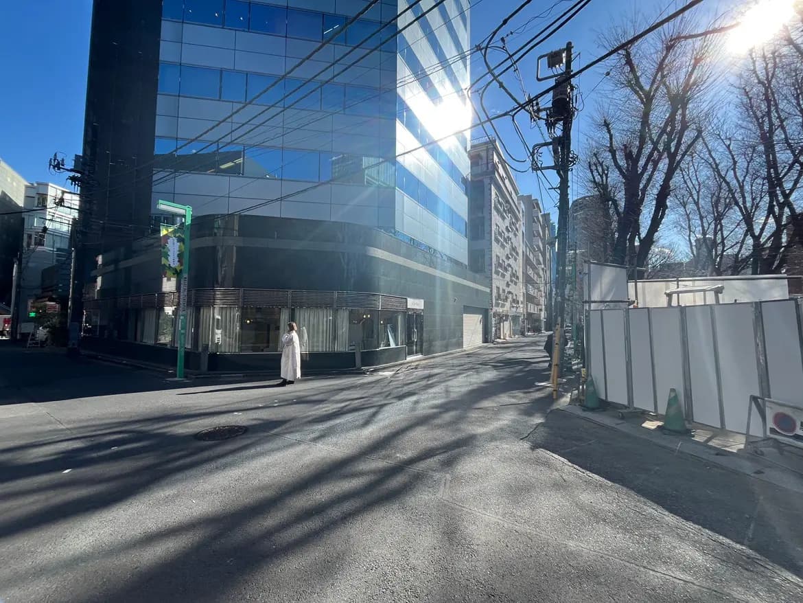 都市の街角でガラス張りのビルと冬の落葉樹、晴れた日の影が映るアスファルト、歩道を歩く人