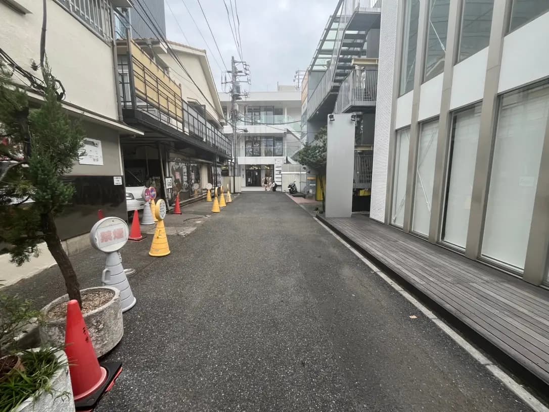 路地に並ぶ店舗と建物、歩道、コーンが設置された市街地の風景