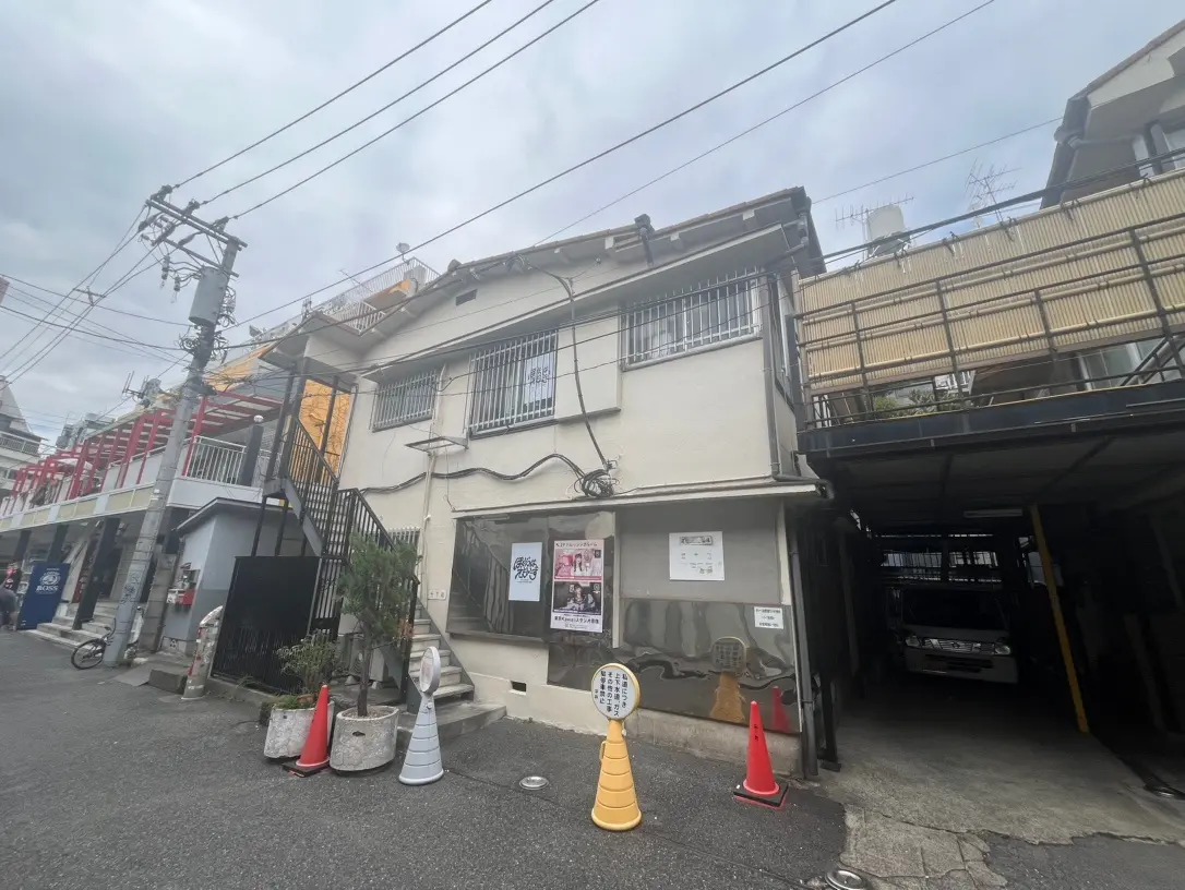 日本の都市部にある伝統的な住宅と駐車スペース、電線が交差する空、広告ポスターが掲示された壁
