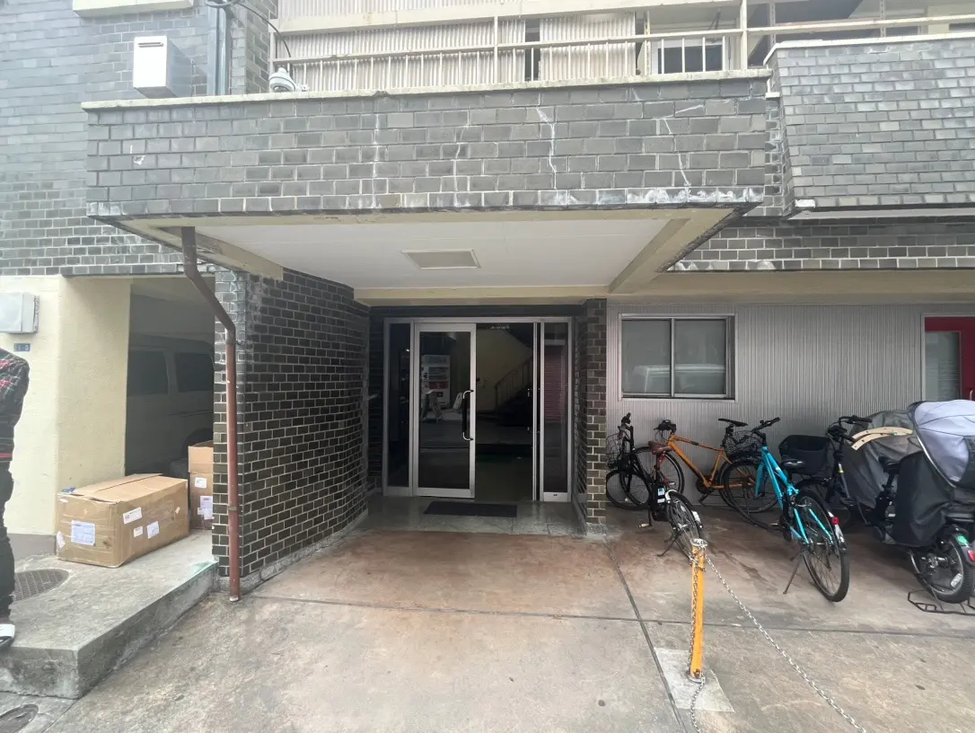 屋根付きの玄関エリア、レンガの壁、自転車が並ぶアパートの入り口