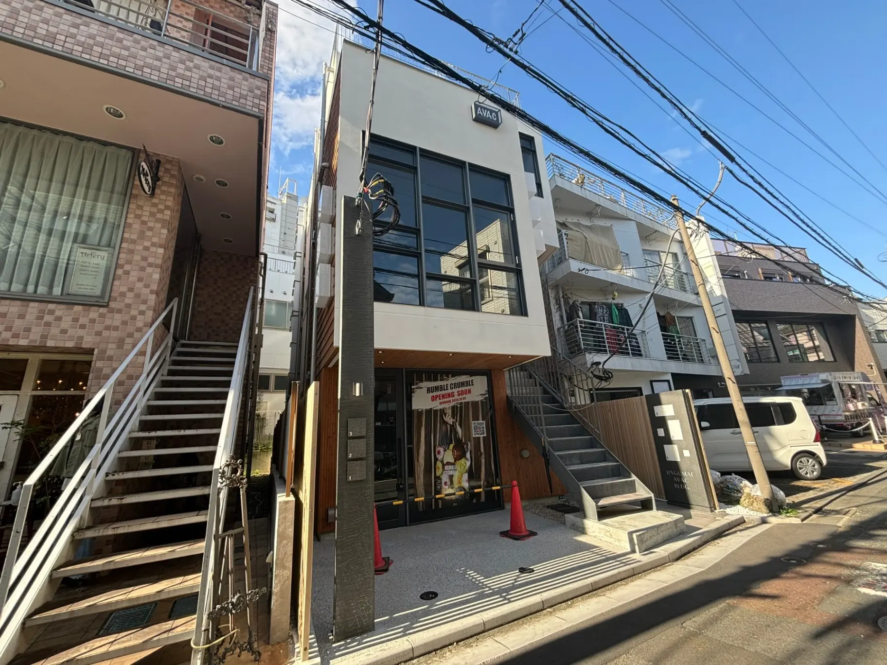 日差しが差し込む市街地の路地にあるモダンなアパート建物と商店、階段と駐車スペースがある外観