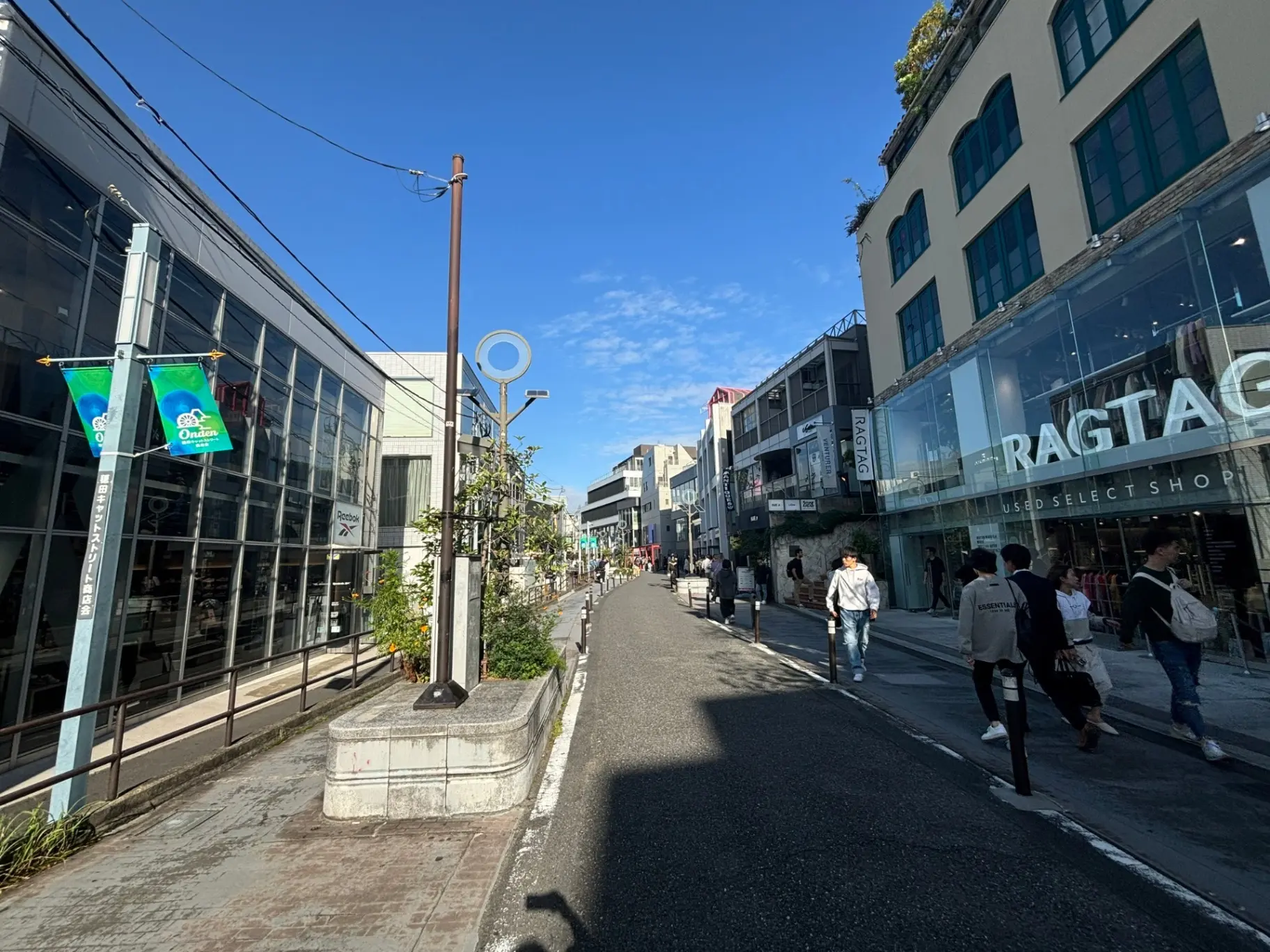 晴れた日の都市のショッピング街、歩行者と店舗が並ぶ通り、青空と都会の風景
