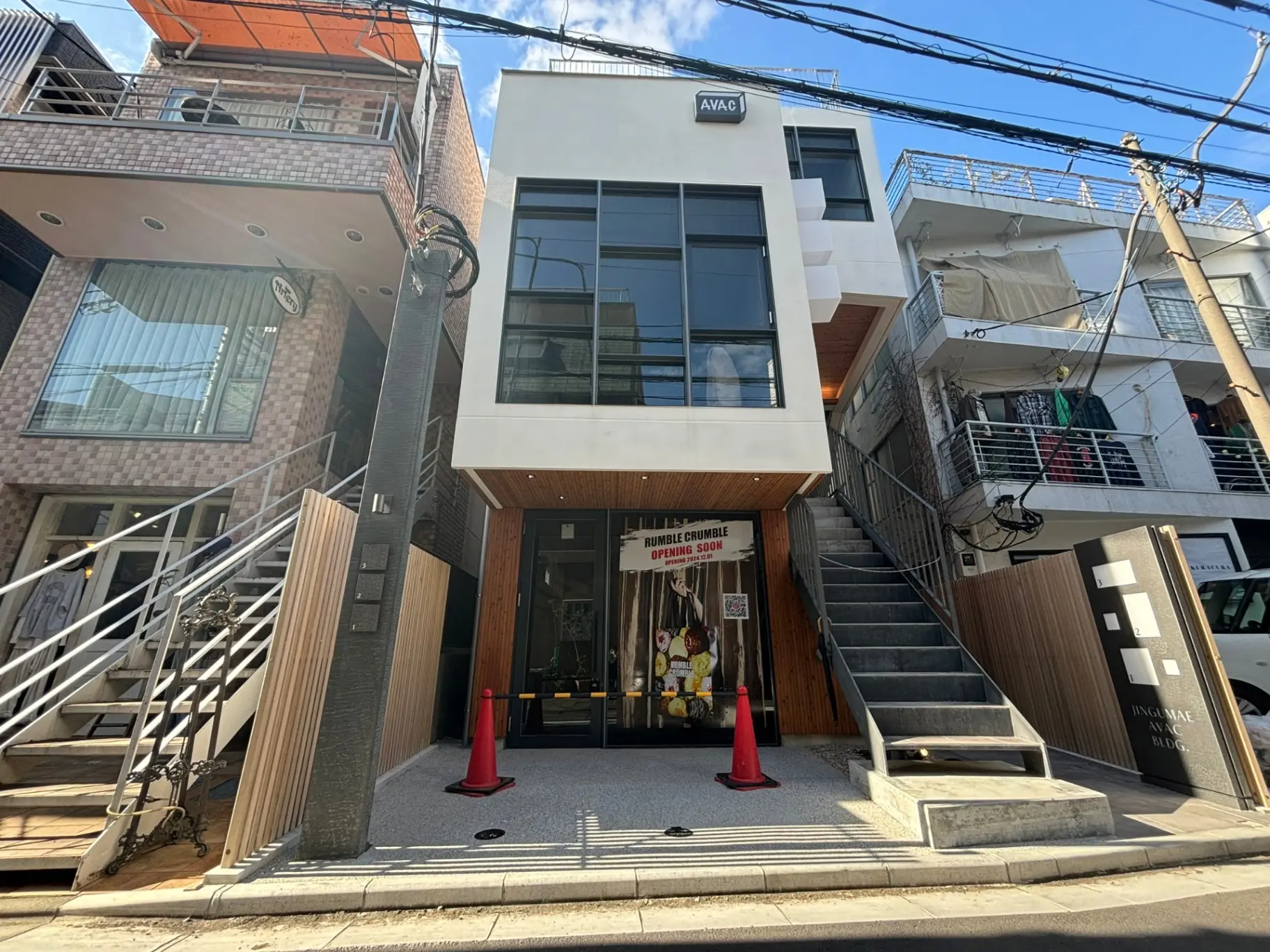 日差しが差し込む都市の歩道に面したモダンな建物の外観、間もなくオープンの店舗と隣接する階段