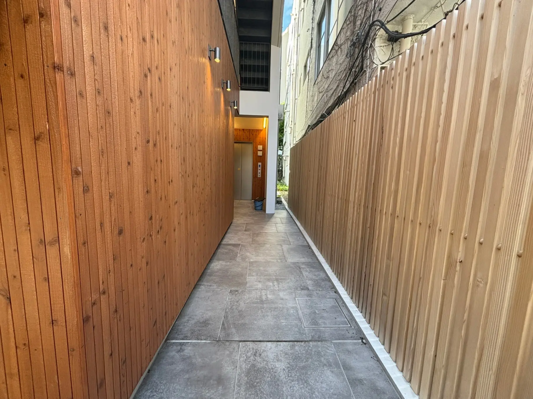 木製の壁に囲まれた狭い通路、コンクリートの歩道、建物へと続く道路