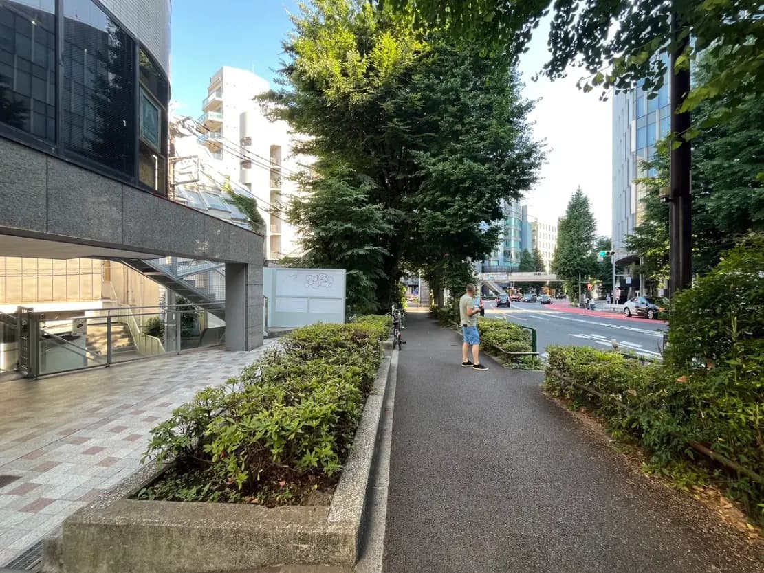 - 都市の歩道、緑豊かな植栽と近代的な建物が並ぶ景観、通りを見つめる人の姿