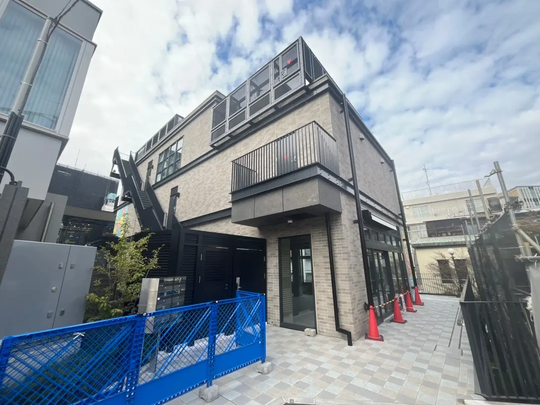 都市の景観に溶け込むモダンな外観の商業ビル、グレーのファサードとブルーのフェンスが特徴的なエントランス