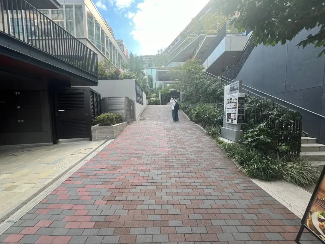 市街地の緑豊かな歩道と赤茶色のレンガの舗道、モダンな建物と外を歩く人