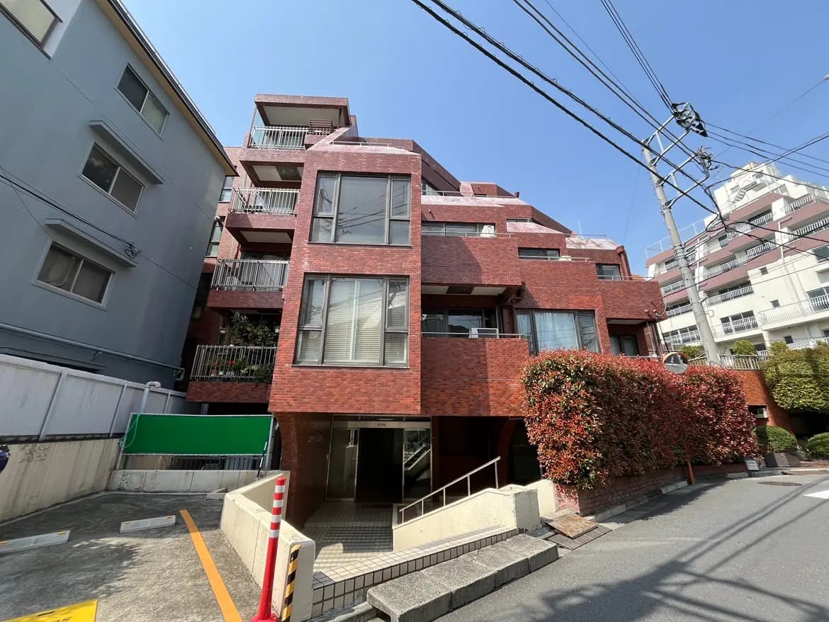 日本の都市部にある赤いレンガ造りのアパートビル、電線が交差する青空、街路樹が見える外観