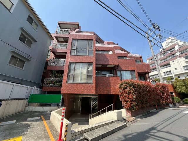 日本の都市部にある赤いレンガ造りのアパートビル、電線が交差する青空、街路樹が見える外観