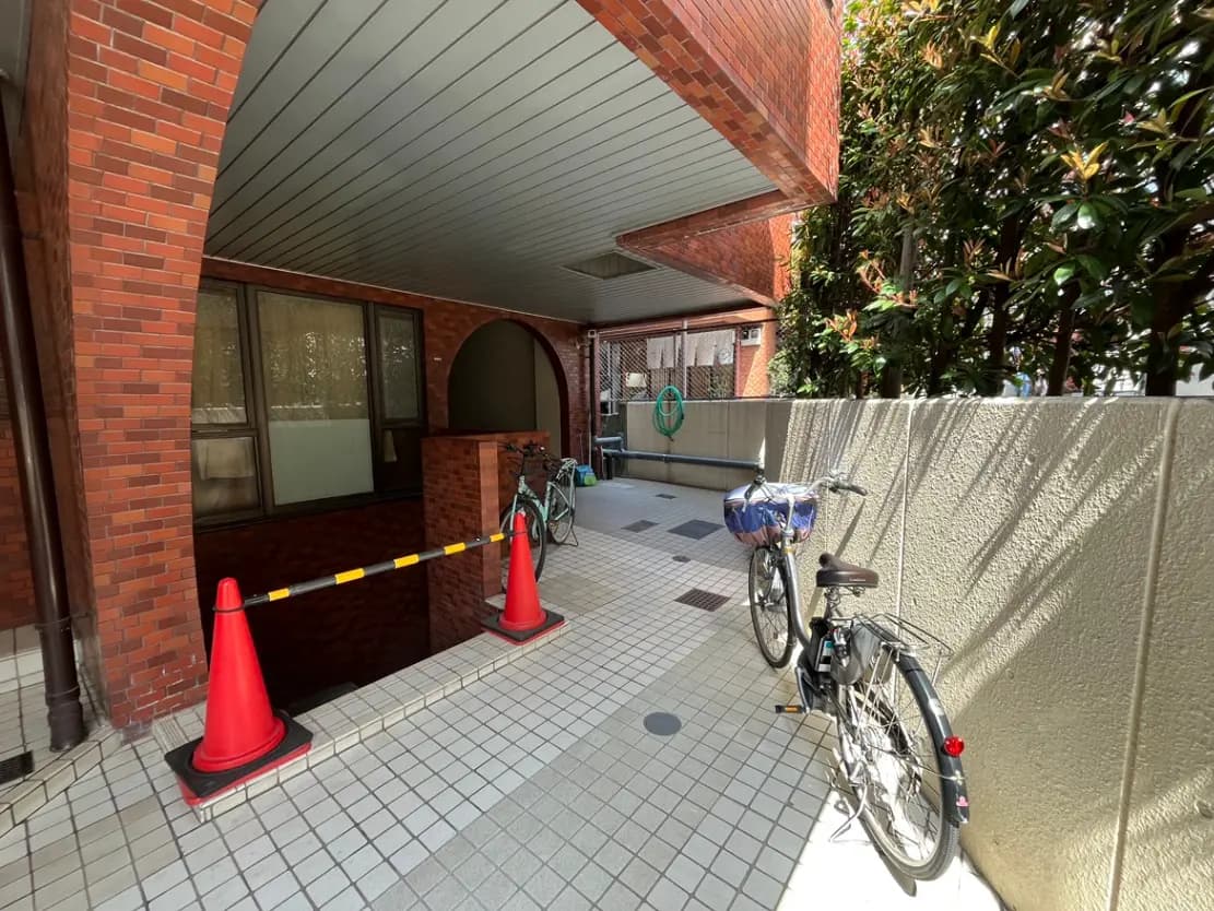 レンガ造りの建物のアーチ型の入り口に設置された自転車駐輪スペース、タイル張りの床と緑豊かな植栽