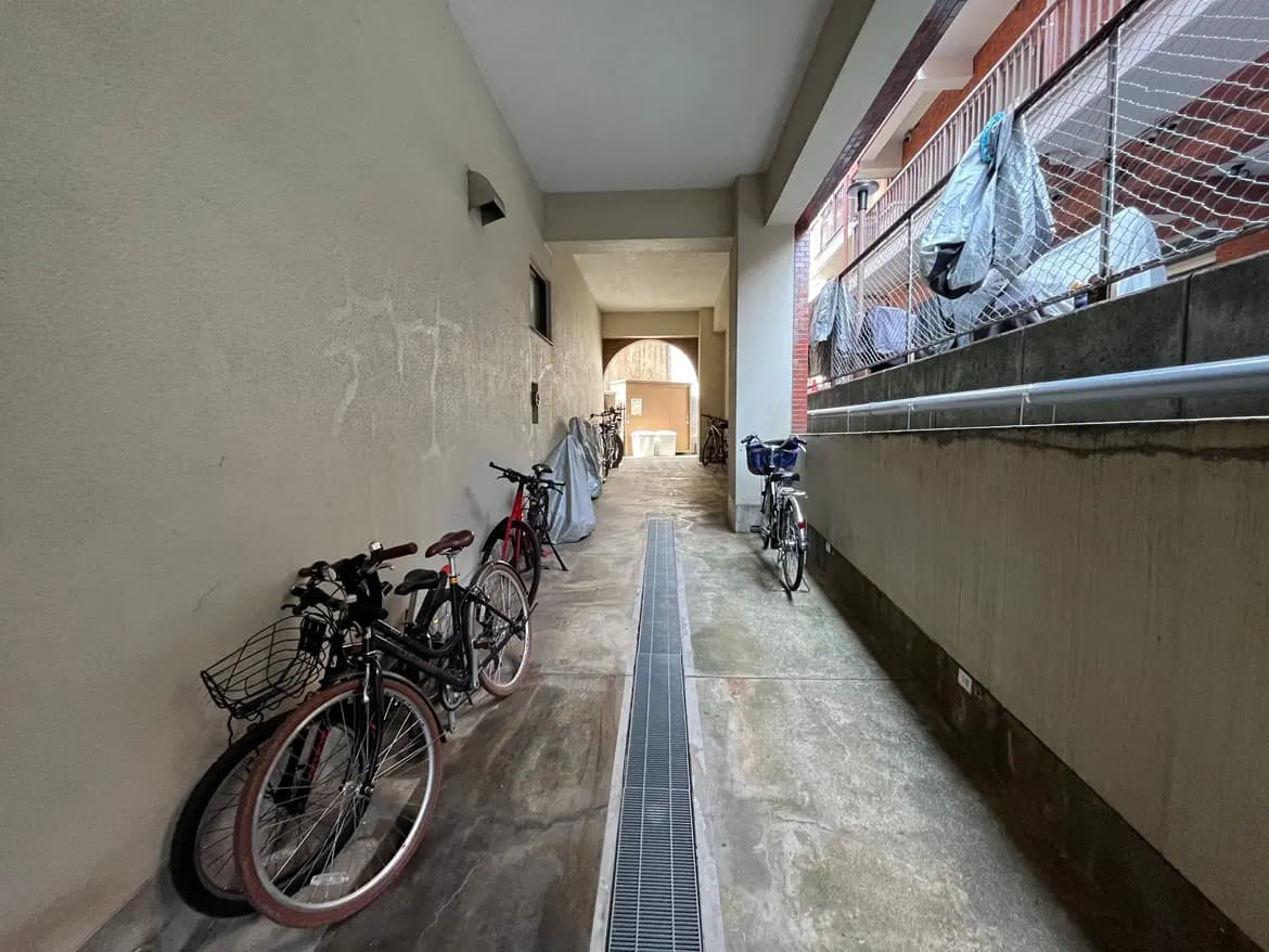 建物の外側にある自転車駐輪スペース、壁には薄汚れあり、カバーをかけた自転車が複数台駐輪されている光景