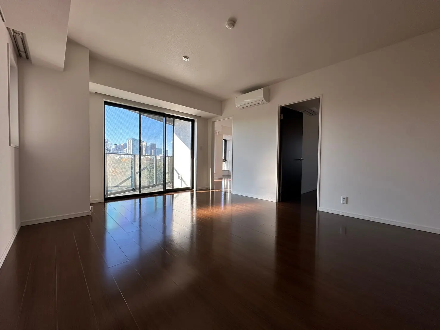 広々とした明るいリビングルーム、木製フローリング、大きな窓と都市の景色