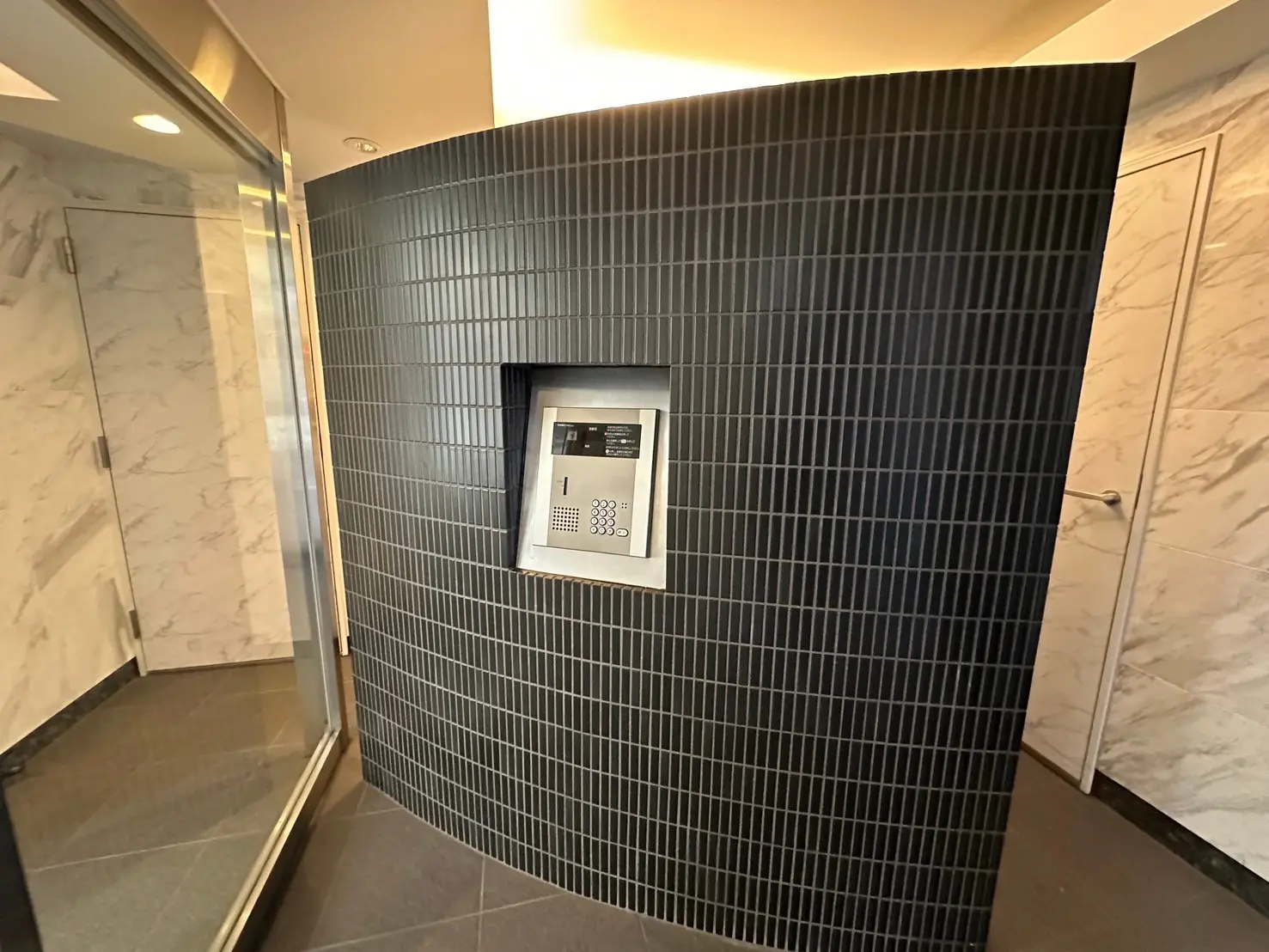 現代的なデザインのオフィスビルのエントランス、丸みを帯びたダークタイルの壁面に取り付けられたインターホン систем