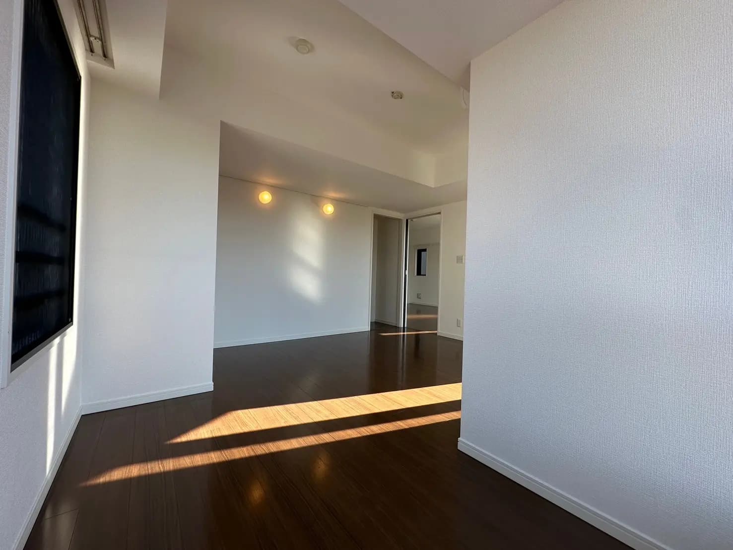 日差しが差し込むモダンなリビングルーム、ダークブラウンのフローリング、白い壁、天井のスポットライト