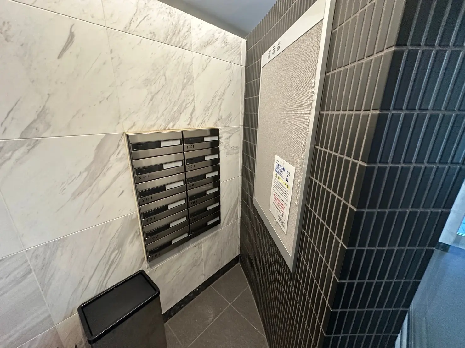 モダンなマンションのエントランスにある郵便受け、大理石調の壁、ダークタイルの装飾