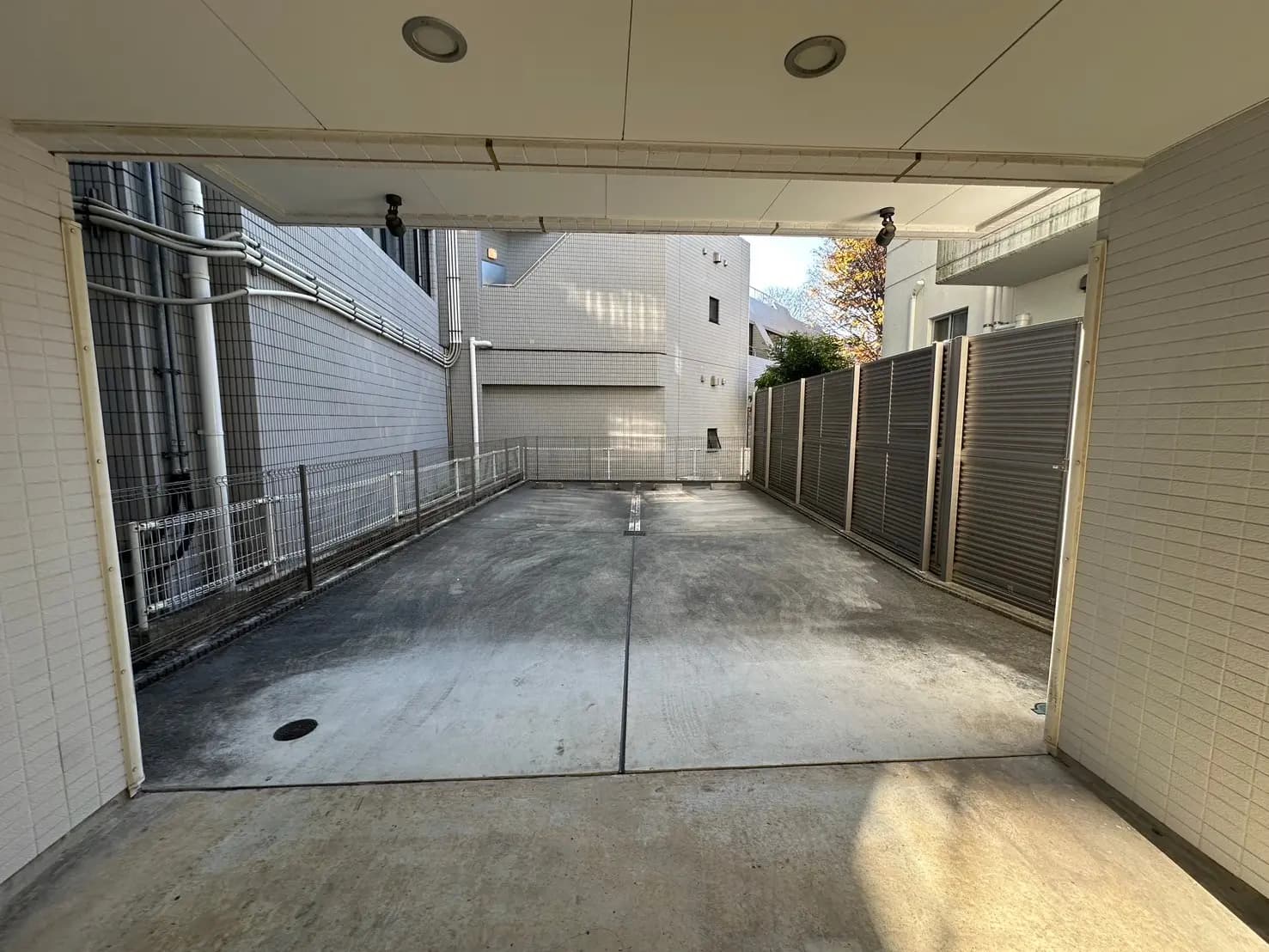 日当たりの良い都市型屋外駐車場、白い壁とモダンな建物、セキュリティフェンス完備