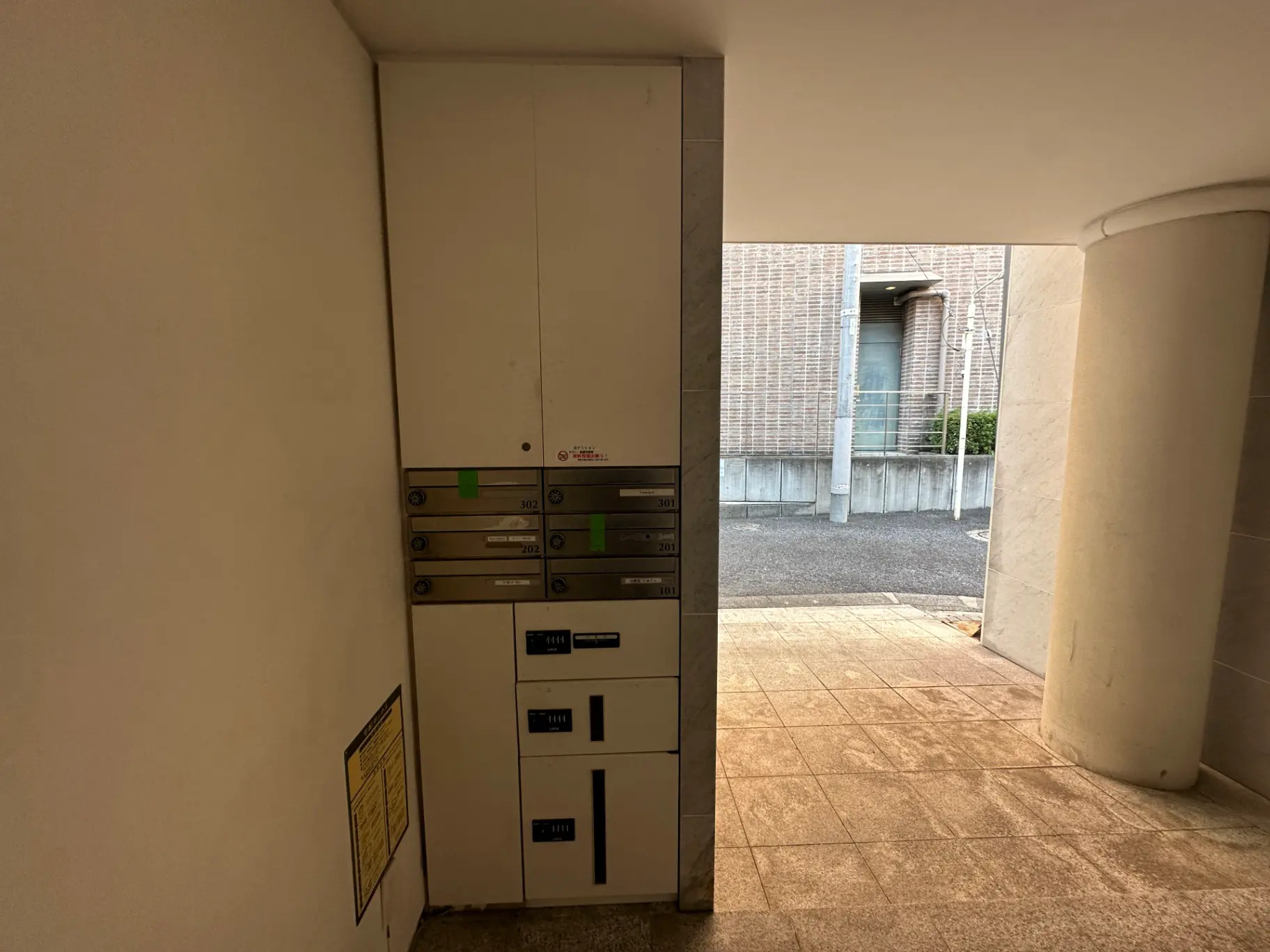 アパートの共有エントランスでの宅配ボックス、クリーム色の壁と円柱、日差しが差し込む外観