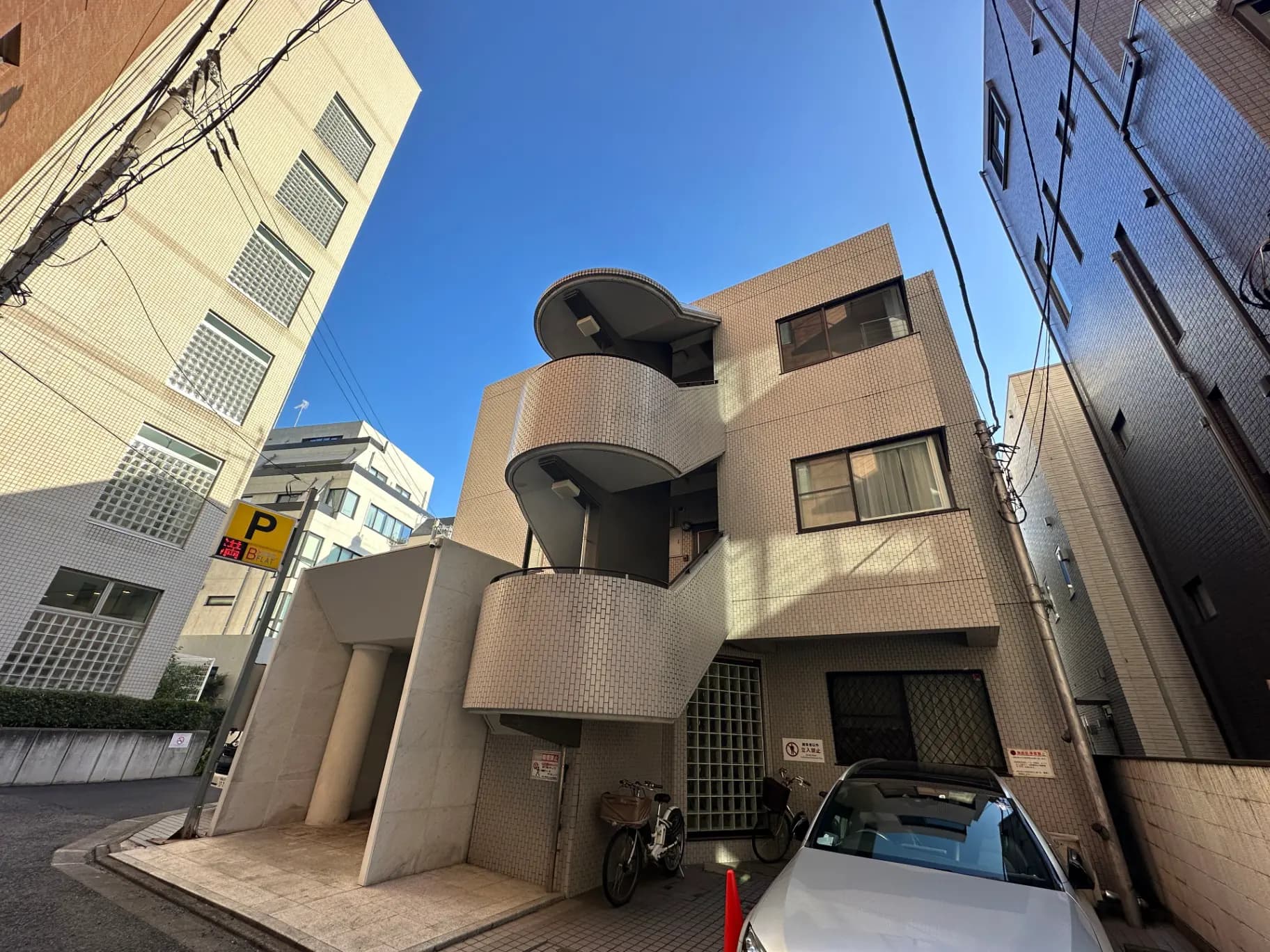 ユニークなデザインの建物と狭い道、青い空と明るい日差し、都市の駐車スペース