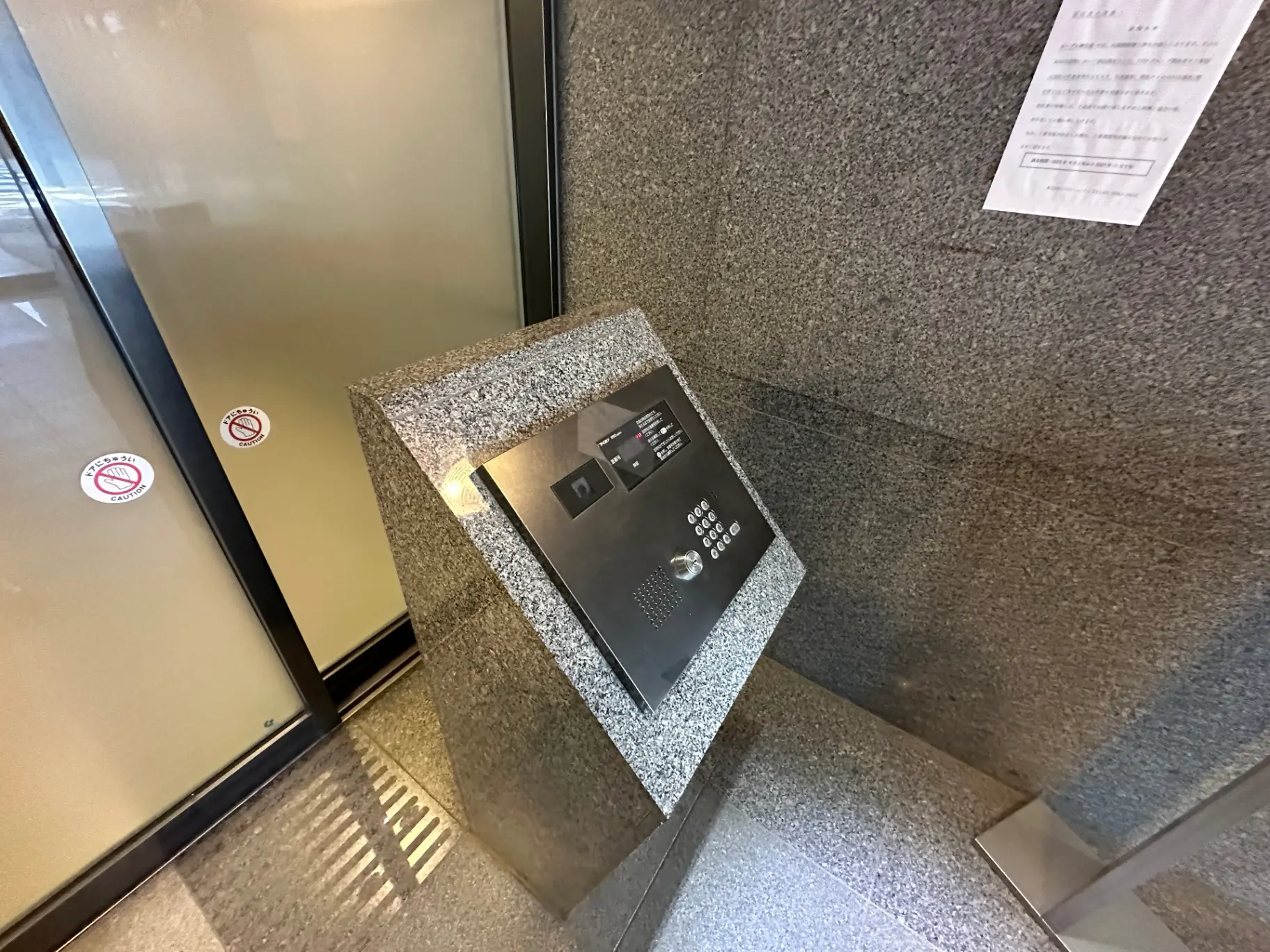 ビルのエントランスに設置された顔認証システムのインターコムと注意書きが貼られた壁