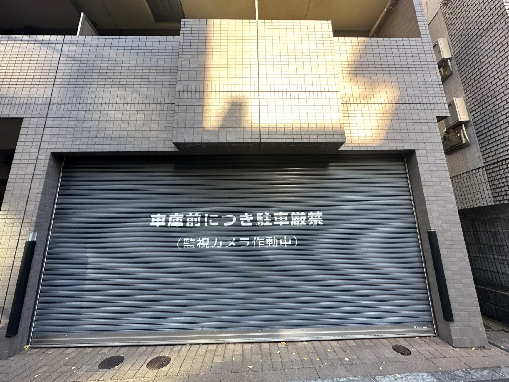 閉まっているシャッター付きのビルの外観、日差しを受けて影が映る都市の風景