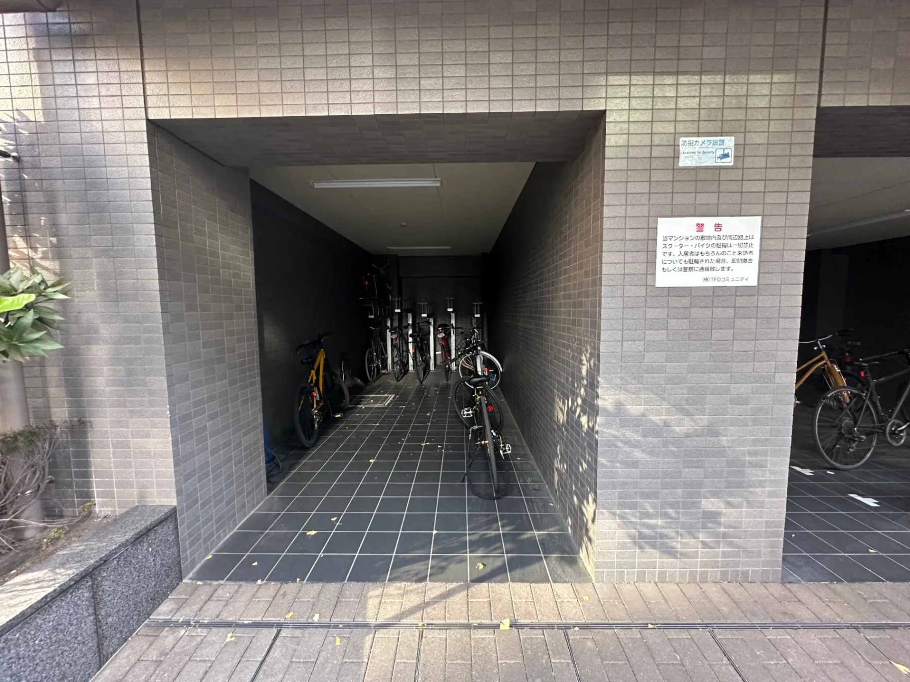建物のアーケード型自転車駐輪場、タイル張りの壁と床、駐輪中の複数の自転車
