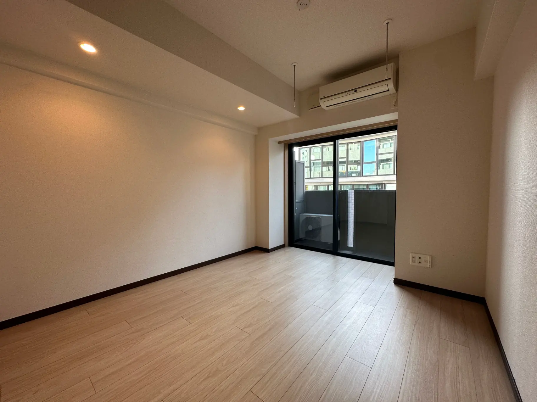 明るく広々とした空き部屋、木目調のフローリングとベランダへの大きな窓, 空調設備付きの現代的なインテリア