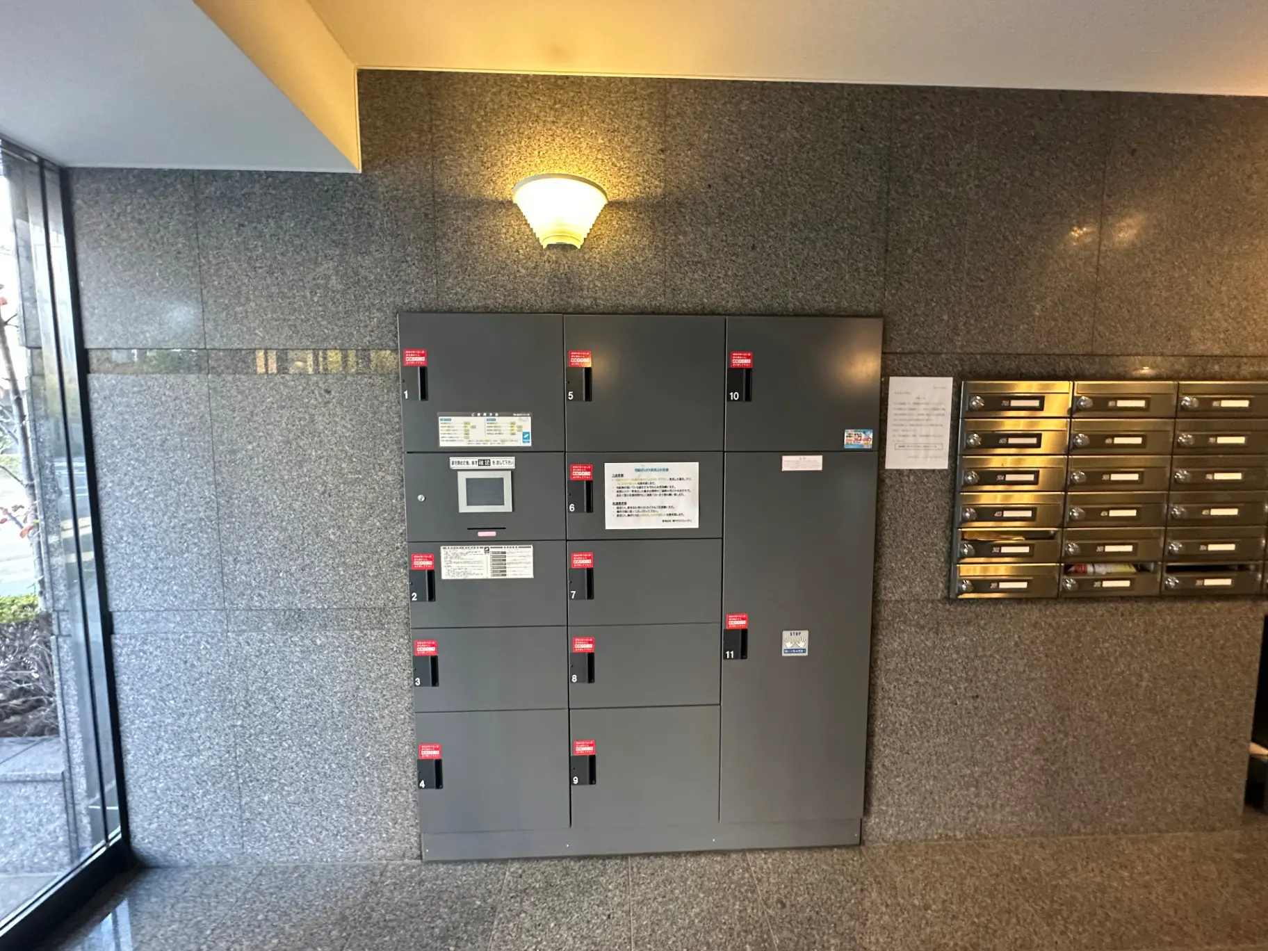宅配ボックスと郵便受けが設置されたマンションのエントランスホール、グレーの壁面と照明