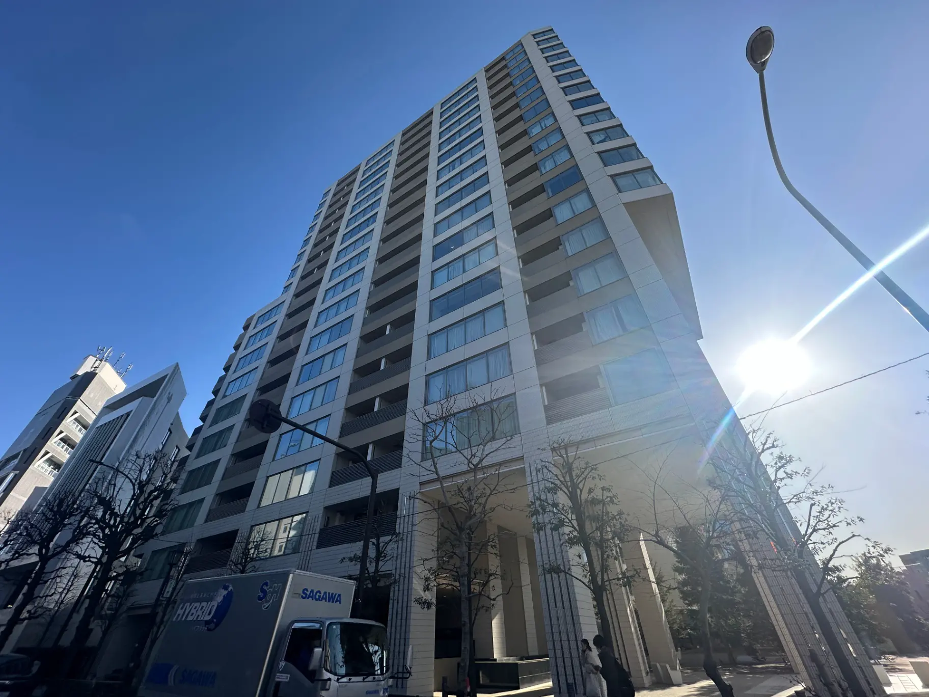 高層マンションの外観、青空と太陽の光、街路樹と街灯がある都会の景観
