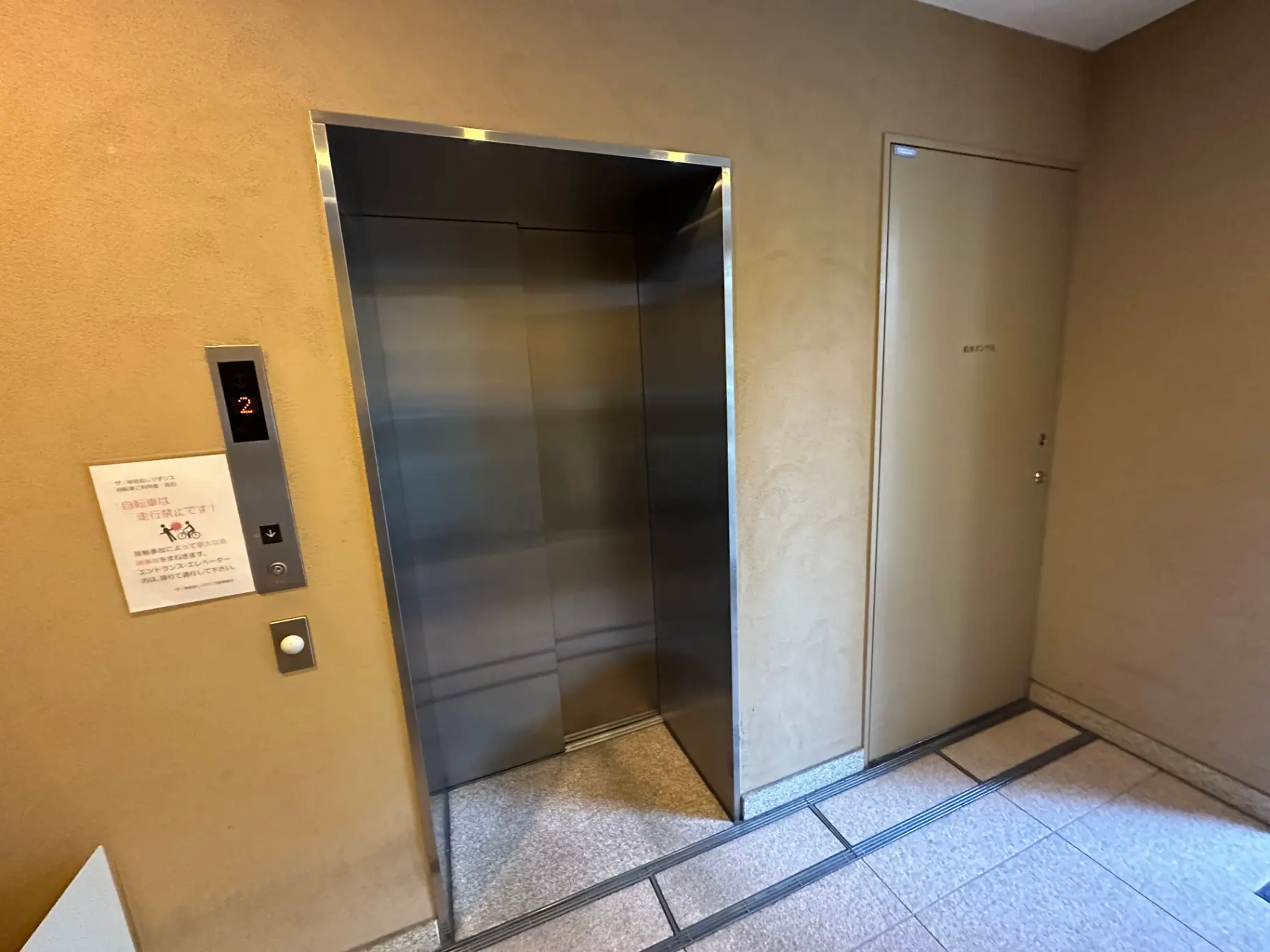 建物内のエレベーターと非常階段の入口、ベージュの壁とタイルの床
