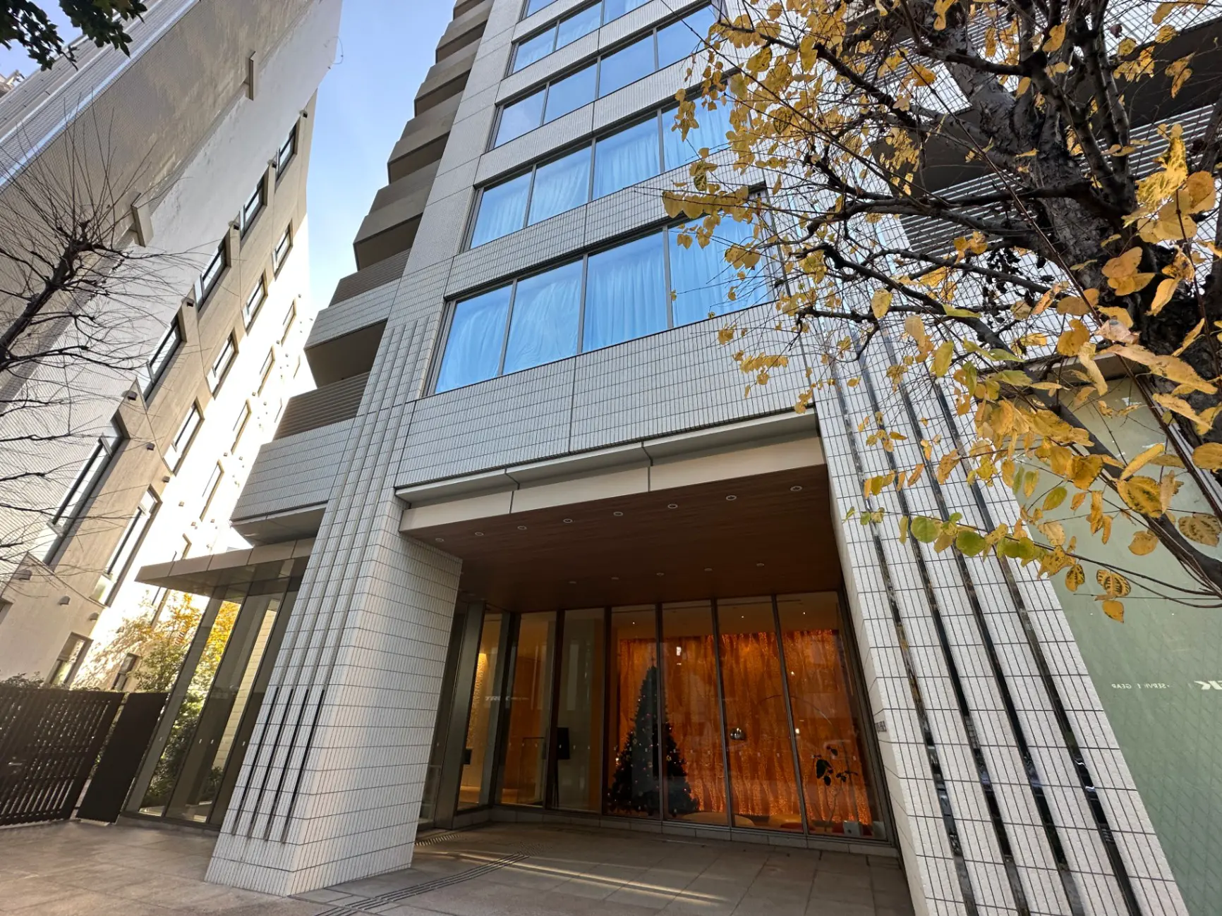 モダンなデザインの都市型アパートメントのエントランス、秋の木々、晴れた日の建物ファサード