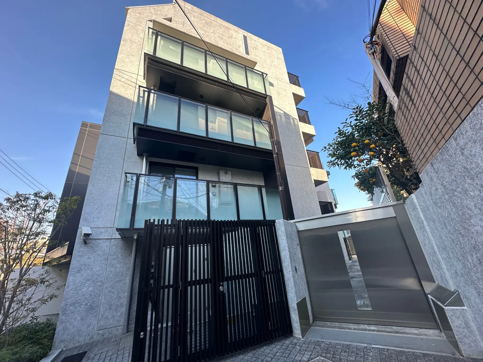 現代的な外装の都市型マンション、クリアな青空に映える建物、ブラックのフェンスとガレージ付き
