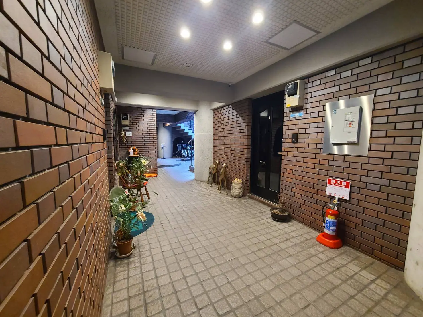 レンガ造りの壁が印象的なマンションのエントランスホール、観葉植物の装飾と防災設備が完備された安全な空間