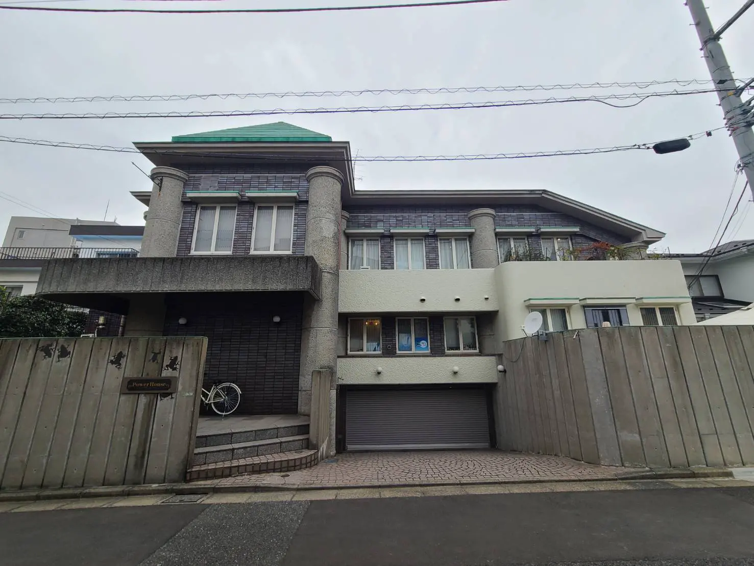 都市部にあるモダンな二階建ての家、ガレージ付き、木製のフェンスと自転車が見える