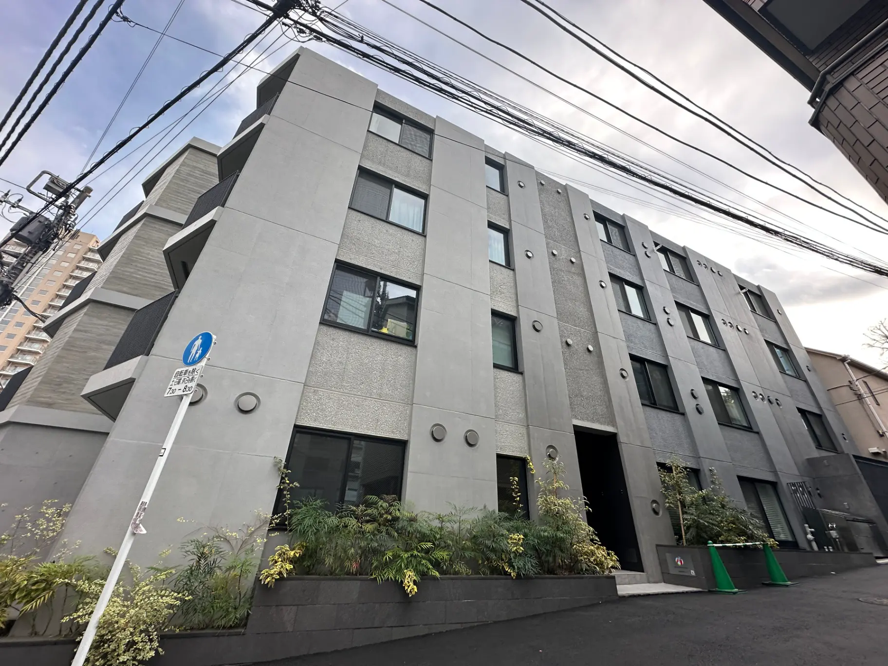 現代的な外観の都市型アパートメント、グレーのファサードに緑の植物がアクセント
