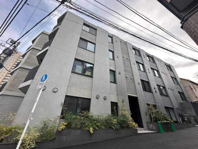 現代的な外観の都市型アパートメント、グレーのファサードに緑の植物がアクセント