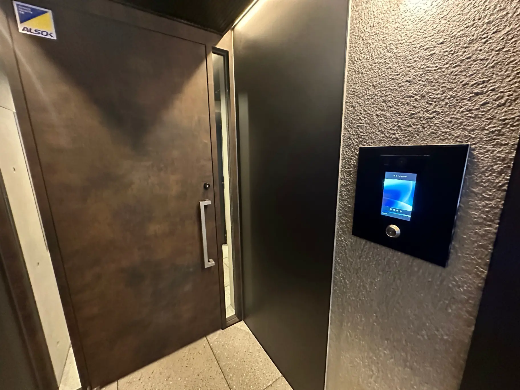 暗い廊下に設置されたモダンなインターホンシステムとセキュリティシステムのロゴがある建物の入口扉